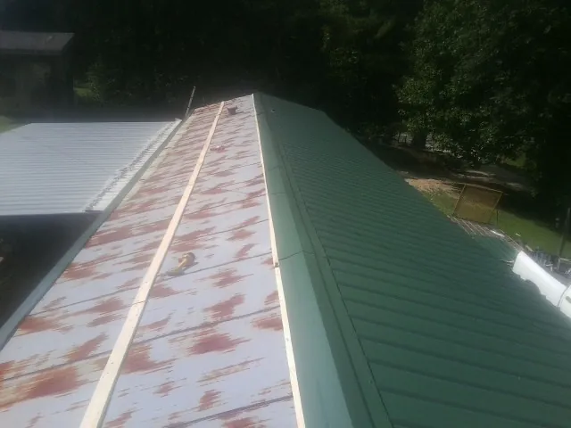 Old rusted panels beside newly installed green metal roofing — Wind Damage Roof Repair by Roofing Brothers in Huntertown