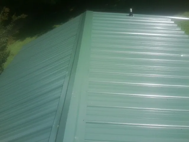 New green metal panels meeting at the ridge of a roof — Flat Roof Repair work by our crew in Huntertown