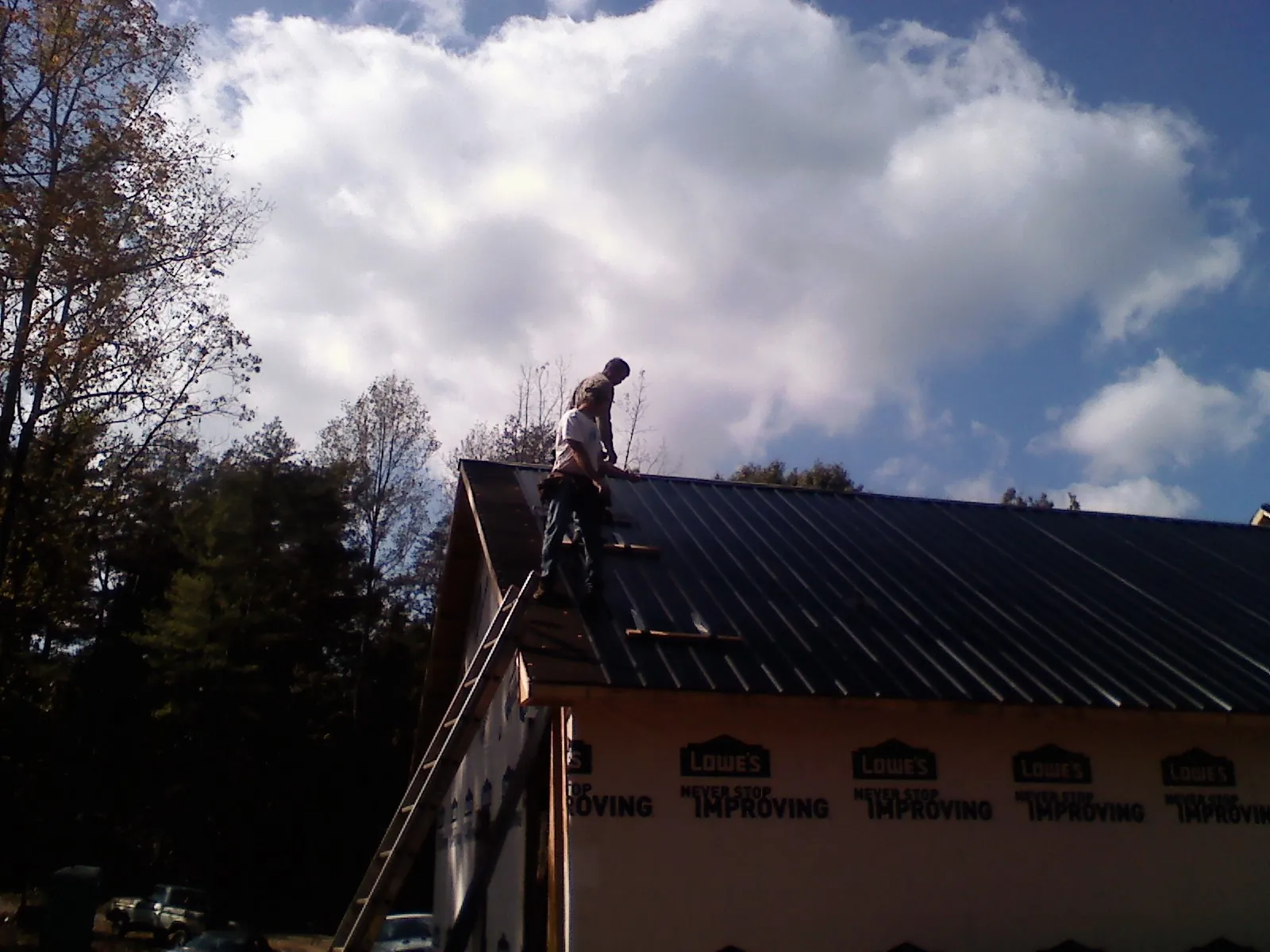 Roofer fastening dark metal panels high against a cloudy sky, from a Roof Inspection job in Huntertown