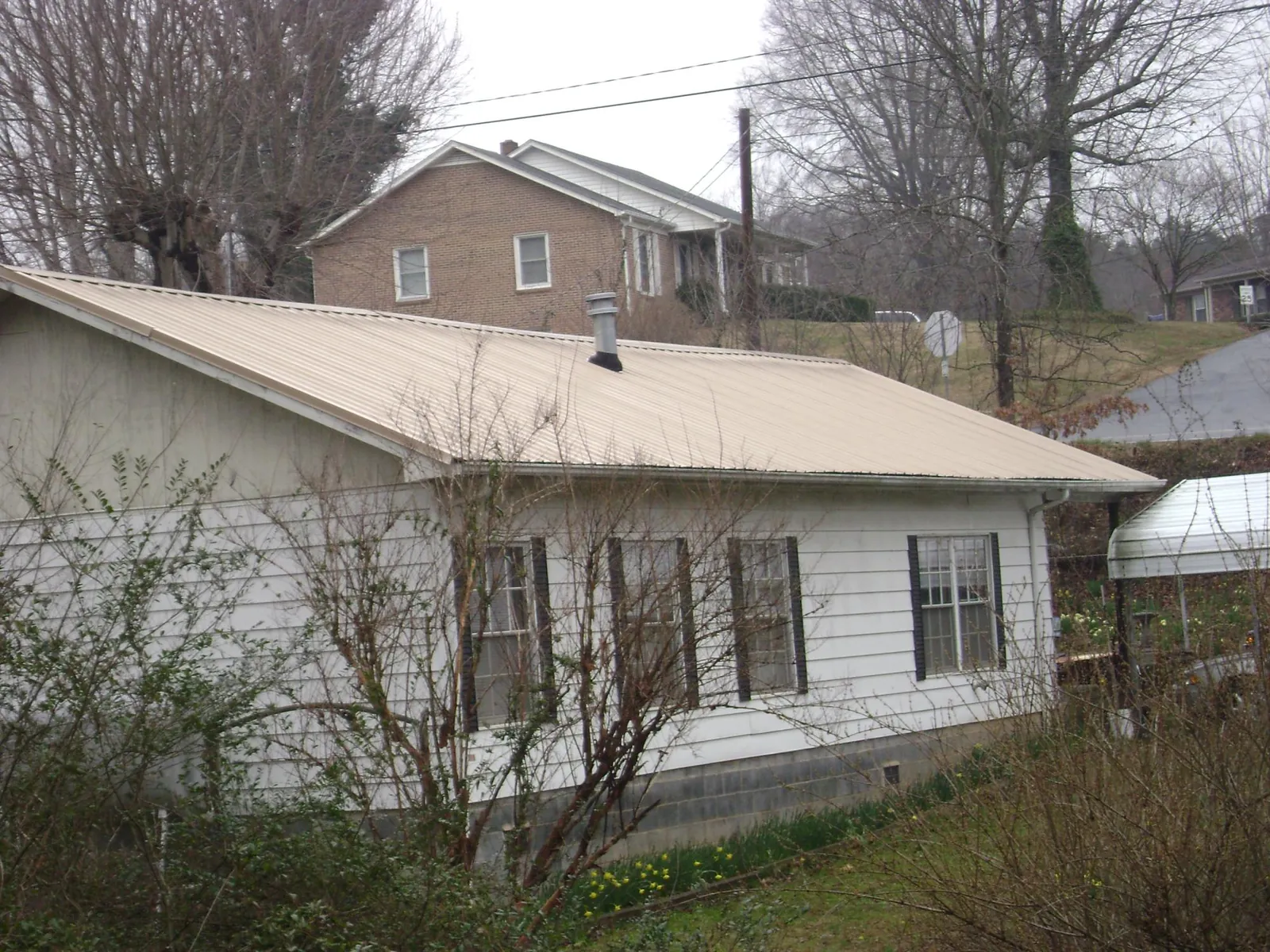 Tan metal roof on a white sided house set into a hillside — Commercial Roofing by Roofing Brothers in Huntertown